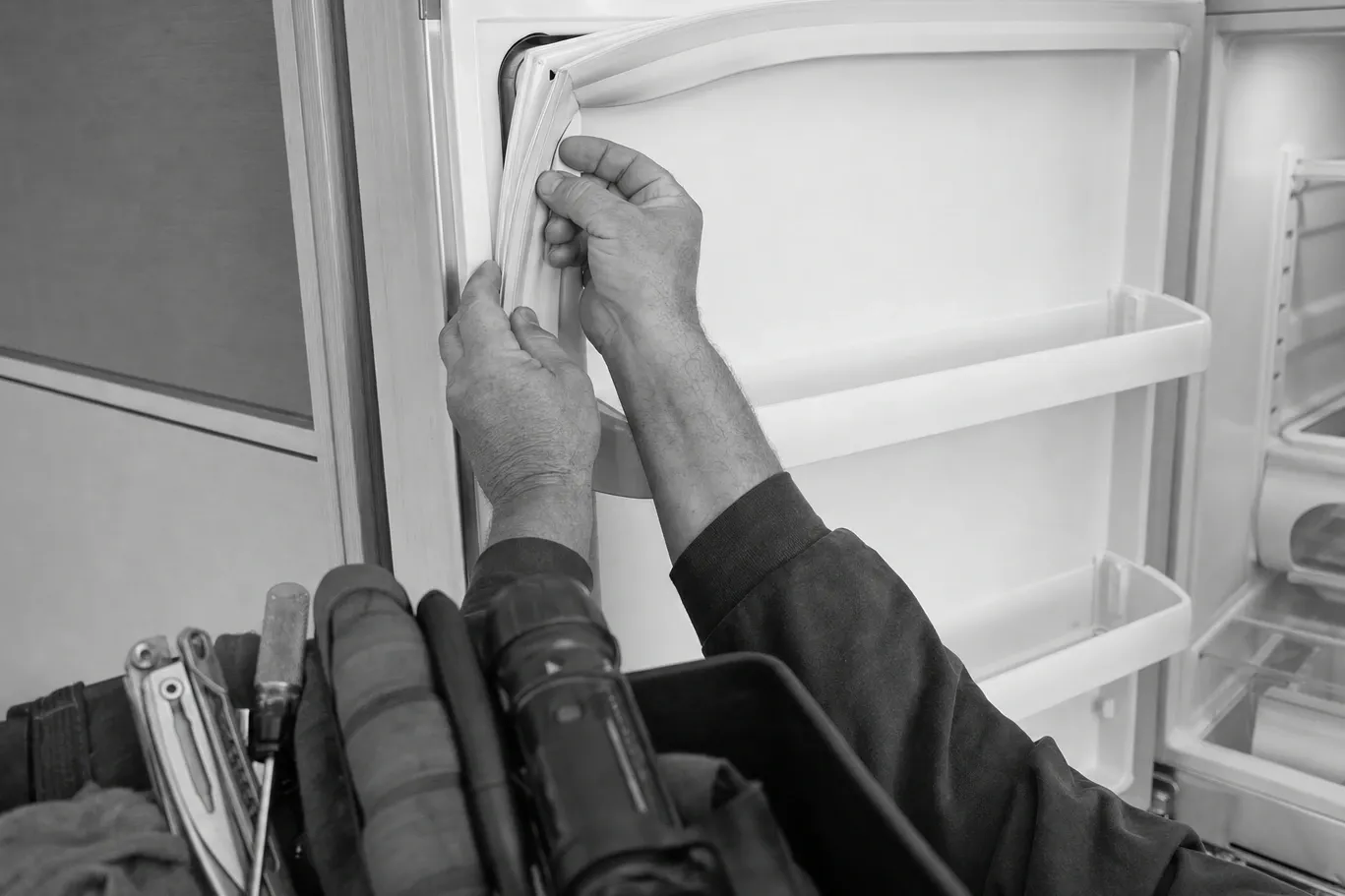 Two hands easing the flexible door gasket back into the channel at the top corner of an open refrigerator door